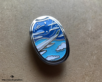 Another product photo of our beautiful day skies window seat hard enamel pin shot at a slanted angle.